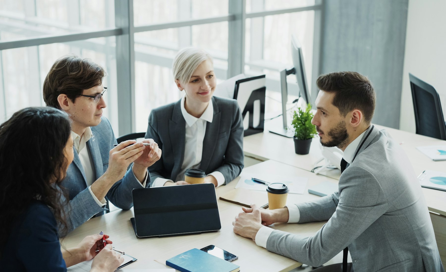 Equipo de trabajo diverso conversando alrededor de una mesa en una oficina luminosa